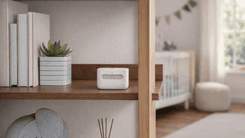 Amazon Smart Air Quality Monitor placed on a wooden shelf in a modern nursery room with plant and crib in background.