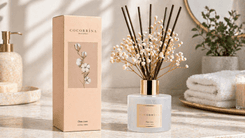 Cocorrína Reed Diffuser Set with clean linen scent, featuring a glass bottle, reed sticks, and dried flowers, displayed on a bathroom countertop beside its packaging and décor items.