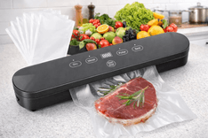 Compact vacuum sealer machine sealing meat with digital controls and food in background